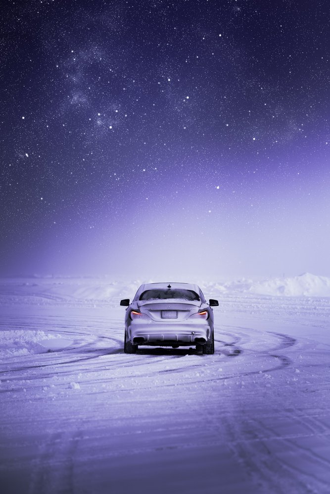 A silver car parked on a snowy landscape under a starry night sky.