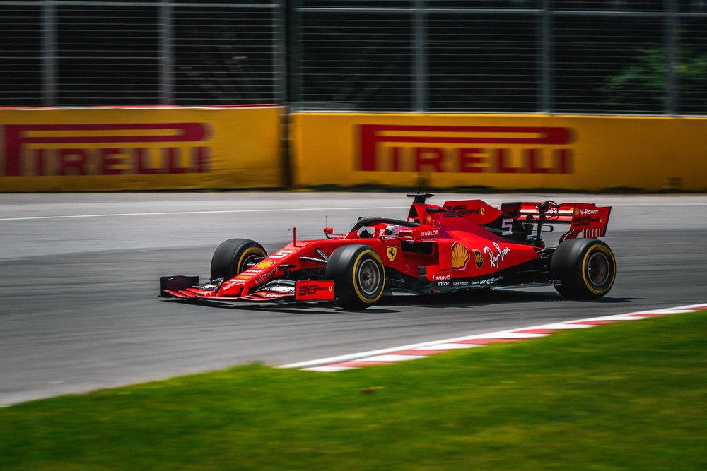 Red Ferrari Formula 1 race car driving on a racetrack with Pirelli barriers in the background.