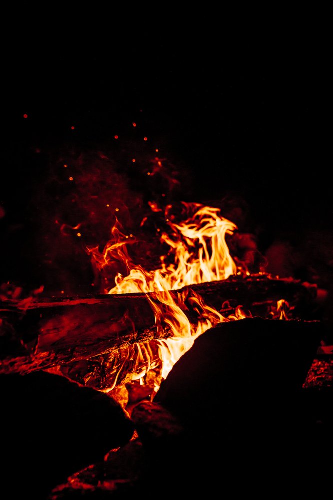 Red flames and burning logs against a dark background.