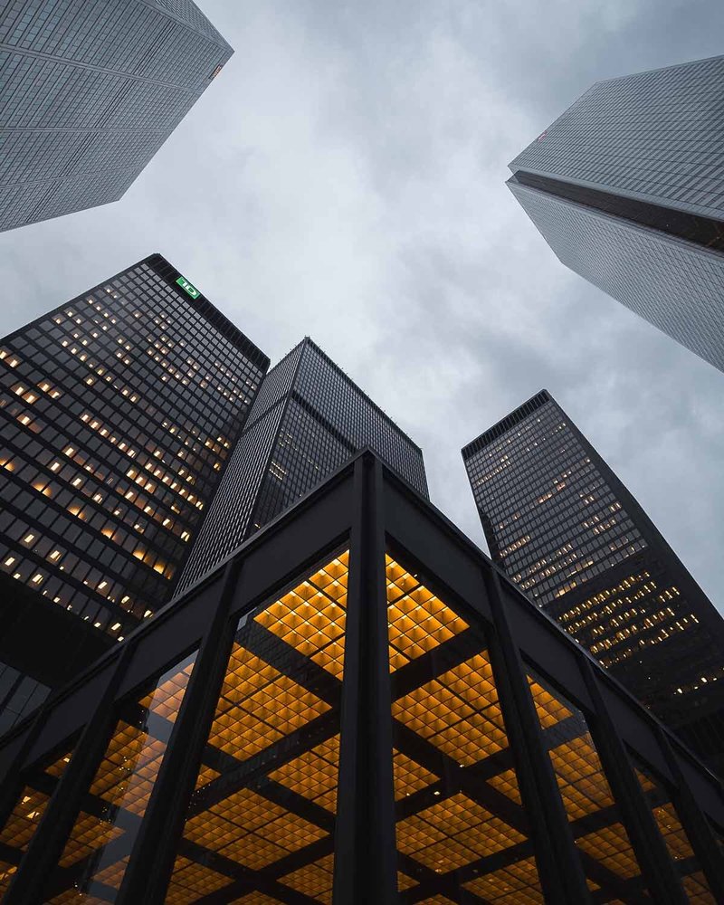 A view looking up at skyscrapers in a city, with a partly cloudy overcast sky.